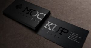 Two overlapping black matte business cards on dark brown surface, MOC logo emblem and KUP lettering.